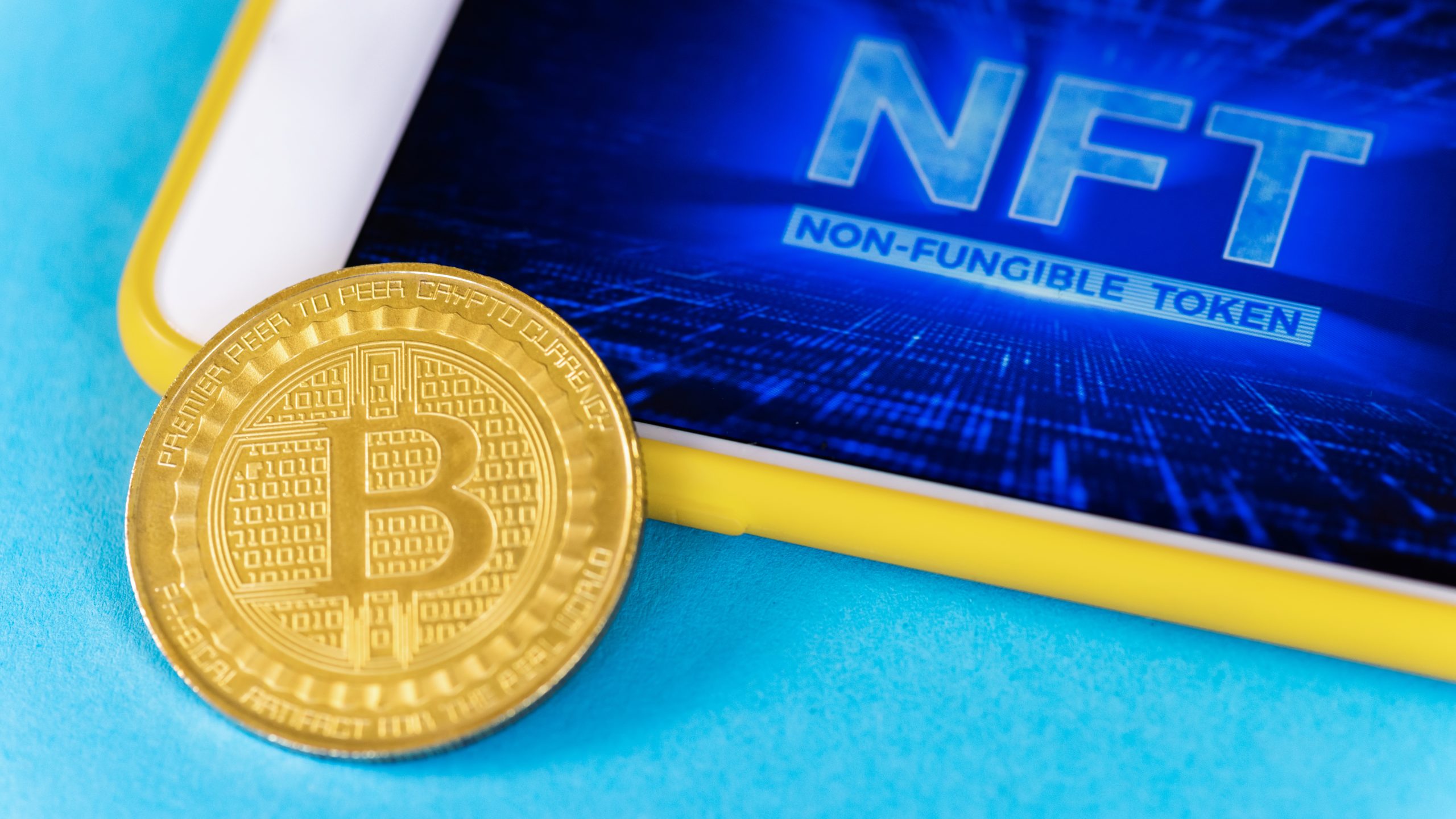Physical Bitcoin gold coin and smartphone with NFT in it, blue background